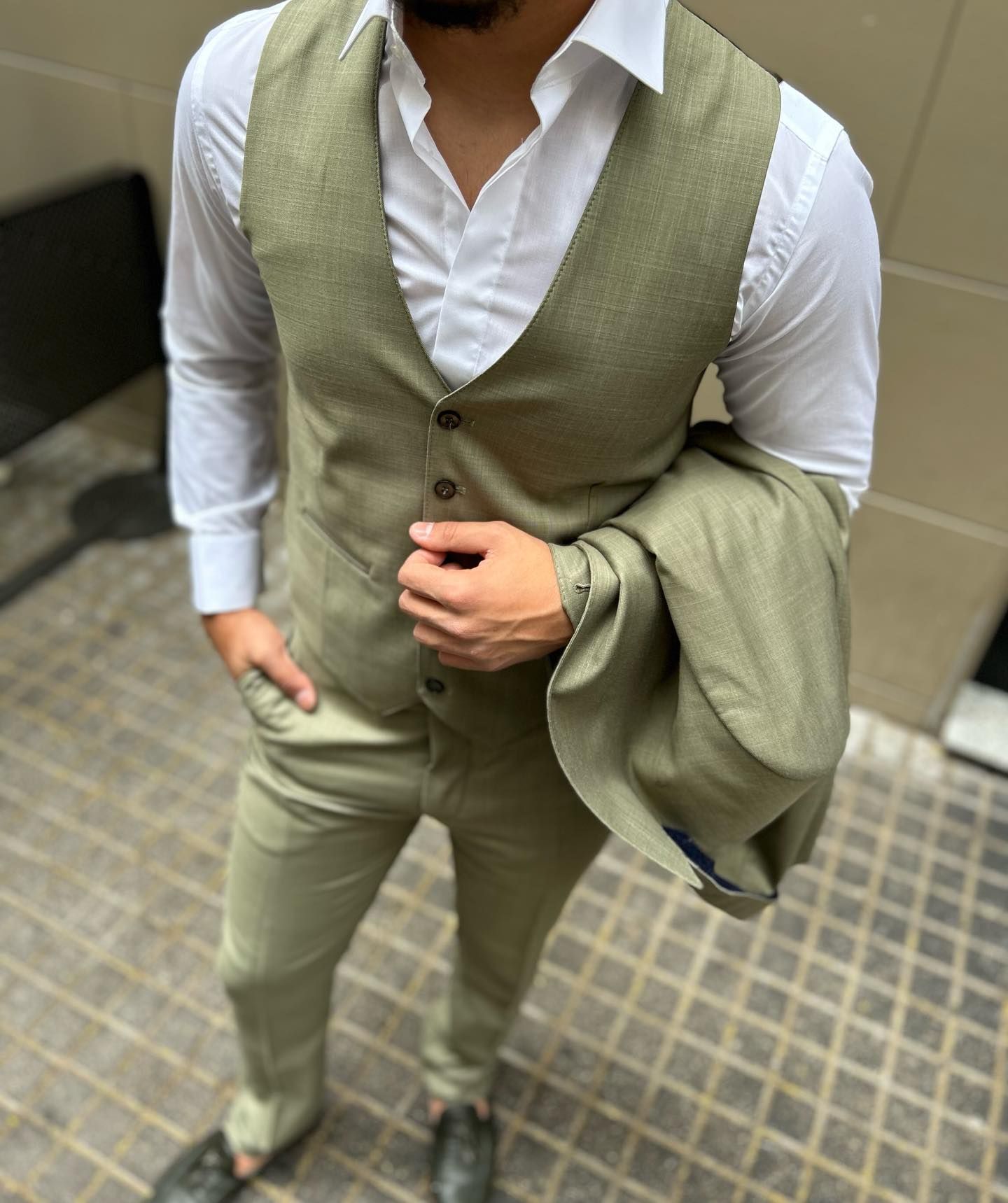 Un hombre que lleva una camisa blanca y un chaleco verde sostiene una chaqueta sobre su hombro.