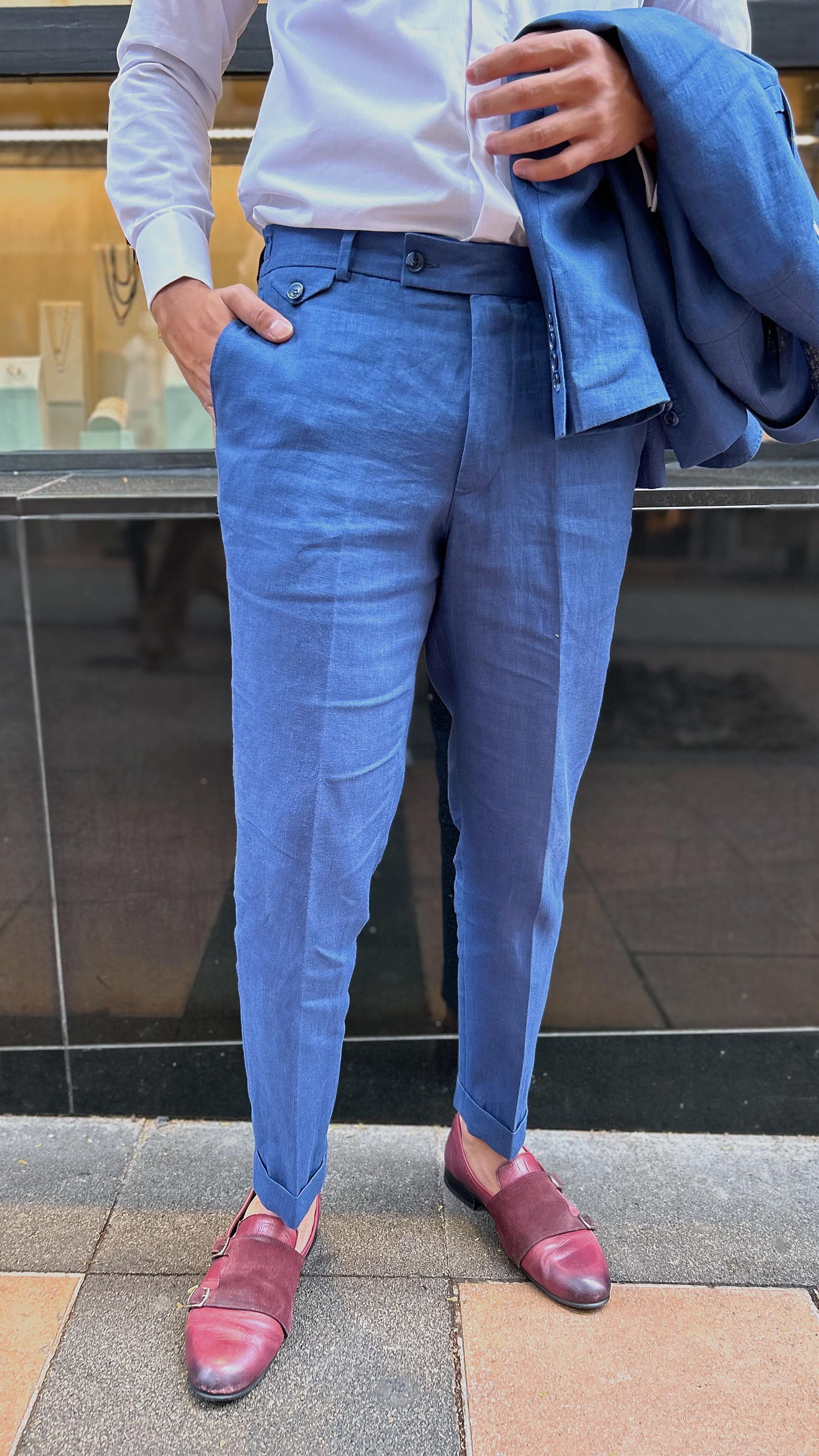 Un hombre que lleva pantalones azules y zapatos rojos está parado en una acera.
