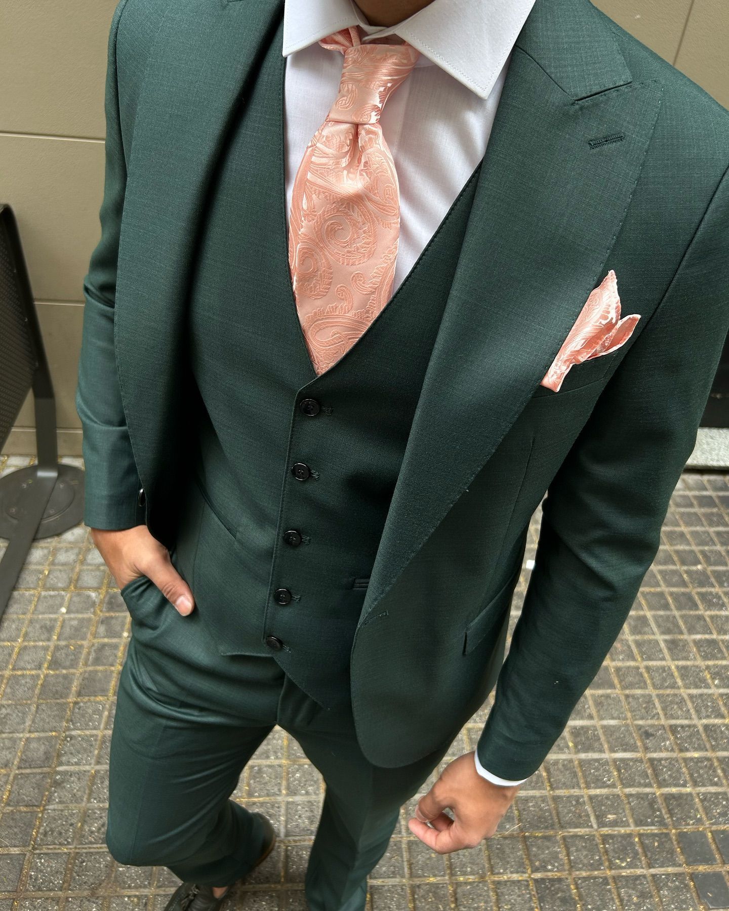 Un hombre con un traje verde, corbata rosa y pañuelo de bolsillo.