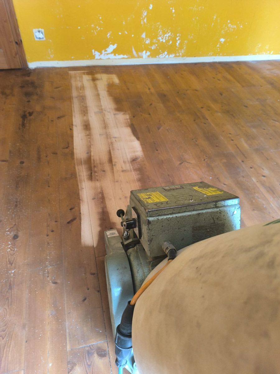 Eine Person schleift einen Holzboden mit einer Maschine.