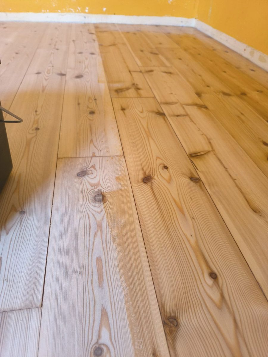 Eine Person schleift einen Holzboden mit einer Maschine.