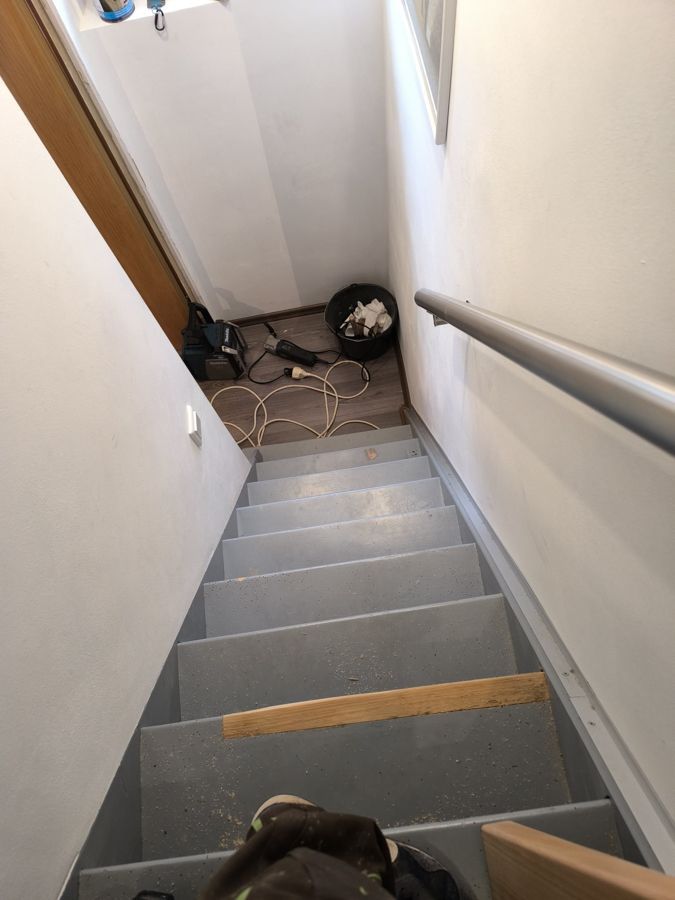 Schmale Treppe mit grauen Stufen, einem silbernen Handlauf und Werkzeugen oben.