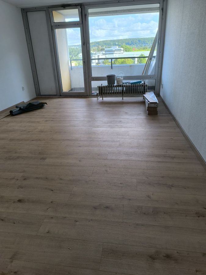 Leerer Raum mit hellbraunem Boden in Holzoptik und großem Fenster mit Blick auf die Stadt.