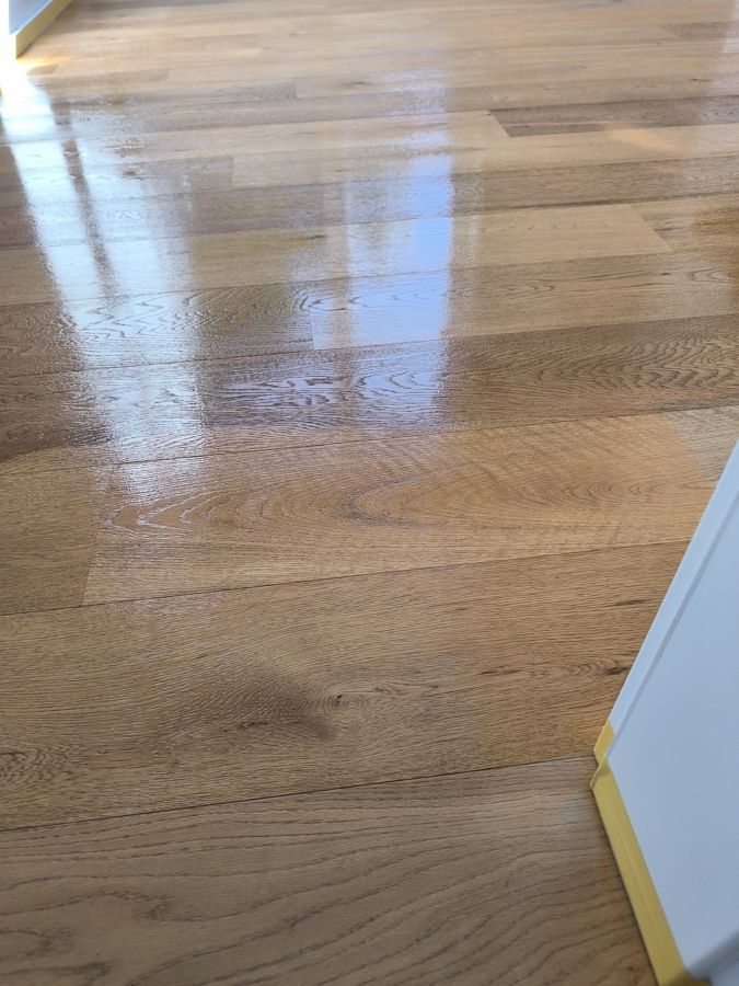 Glänzender Holzboden mit sichtbarer Maserung und Lichtreflexen.