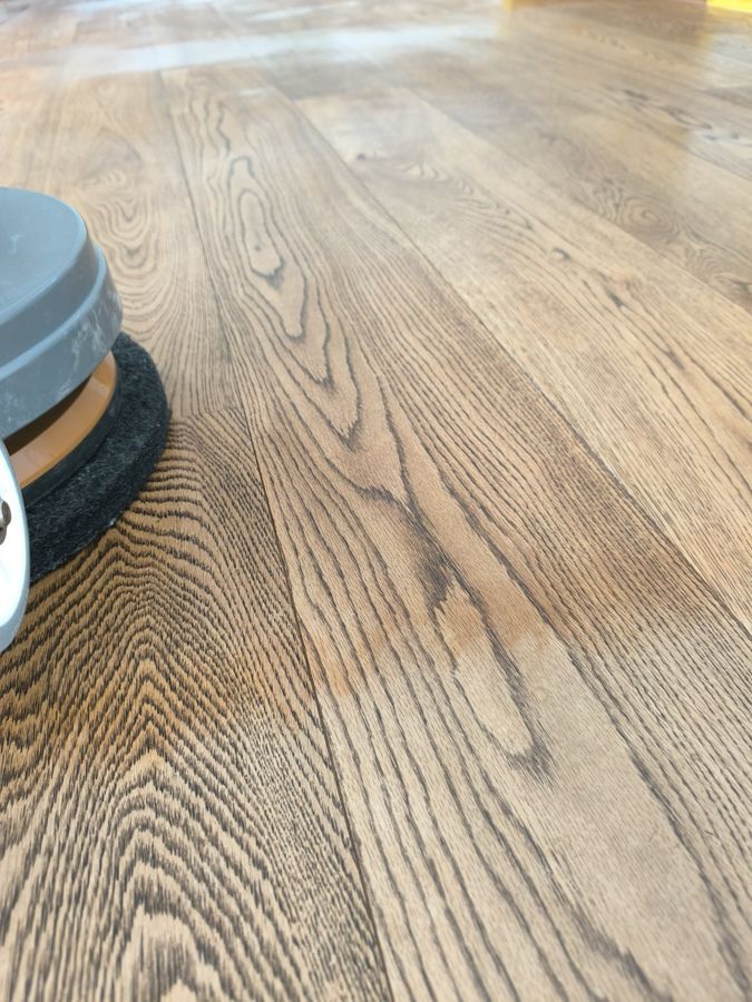 Holzboden wird mit einer Bodenpoliermaschine gereinigt; Nahaufnahme von Maserung und Struktur.