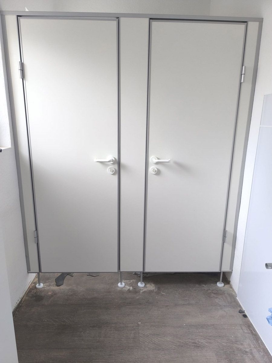 Eine Toilettenkabine mit zwei weißen Türen und Teppichboden.