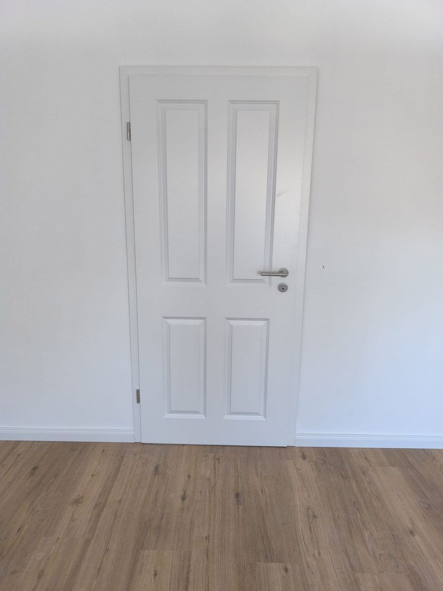 Ein leerer Raum mit einer weißen Tür und einem Holzboden.
