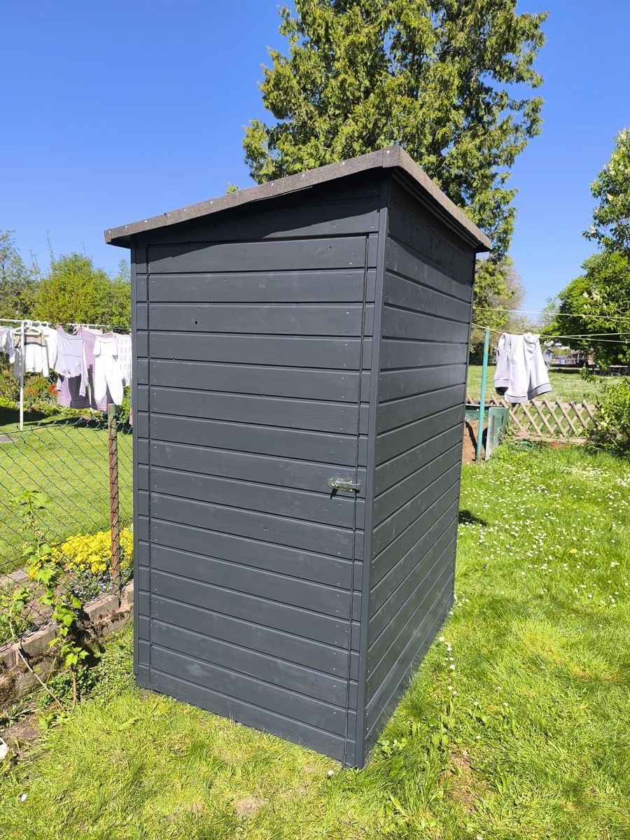 Inmitten eines üppigen grünen Feldes steht ein kleiner schwarzer Schuppen.