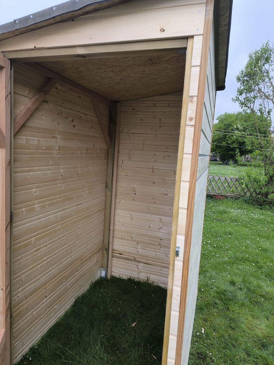 Mitten auf einer Wiese steht ein Holzschuppen.