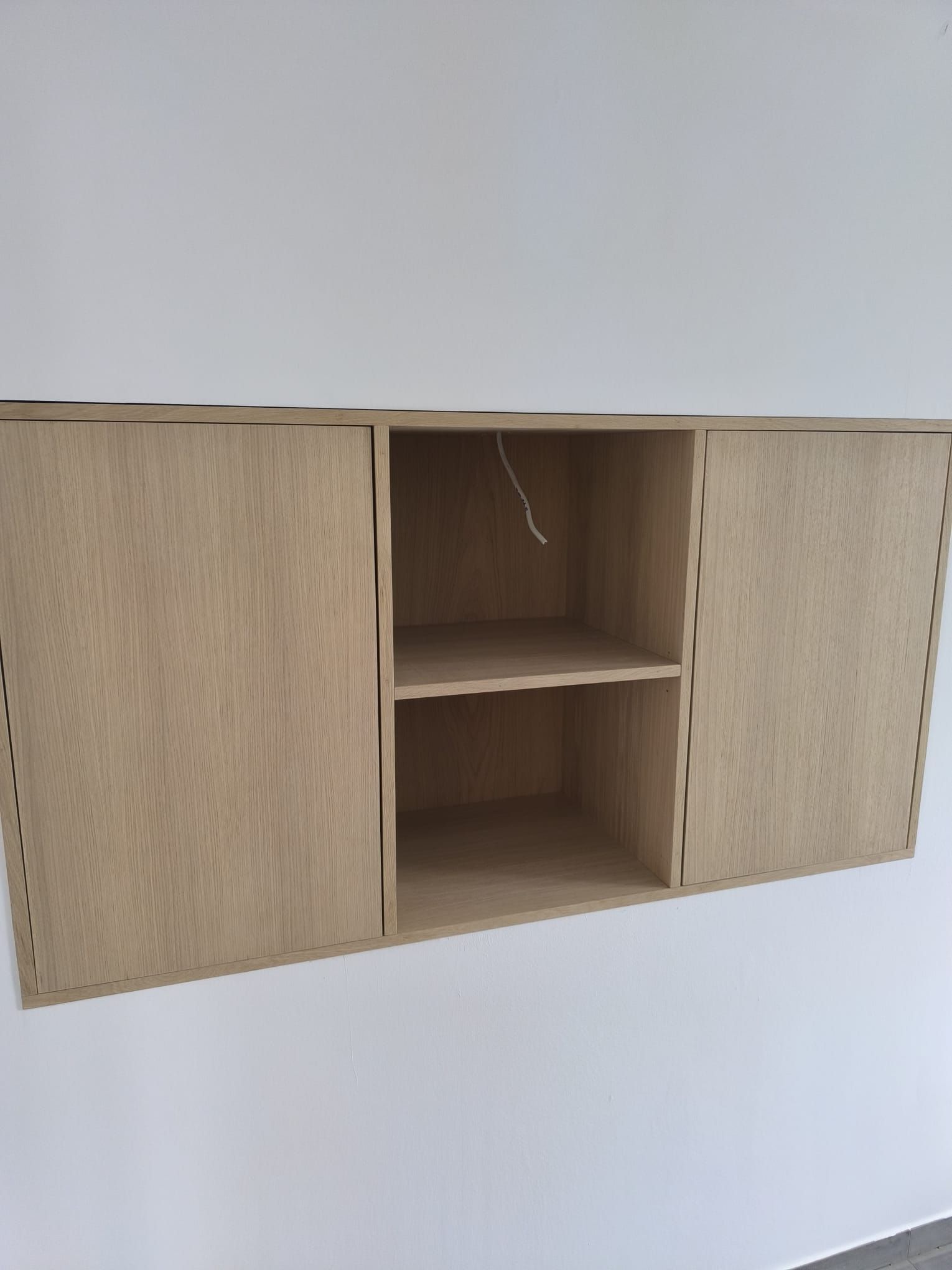 An einer weißen Wand hängt ein Holzregal.