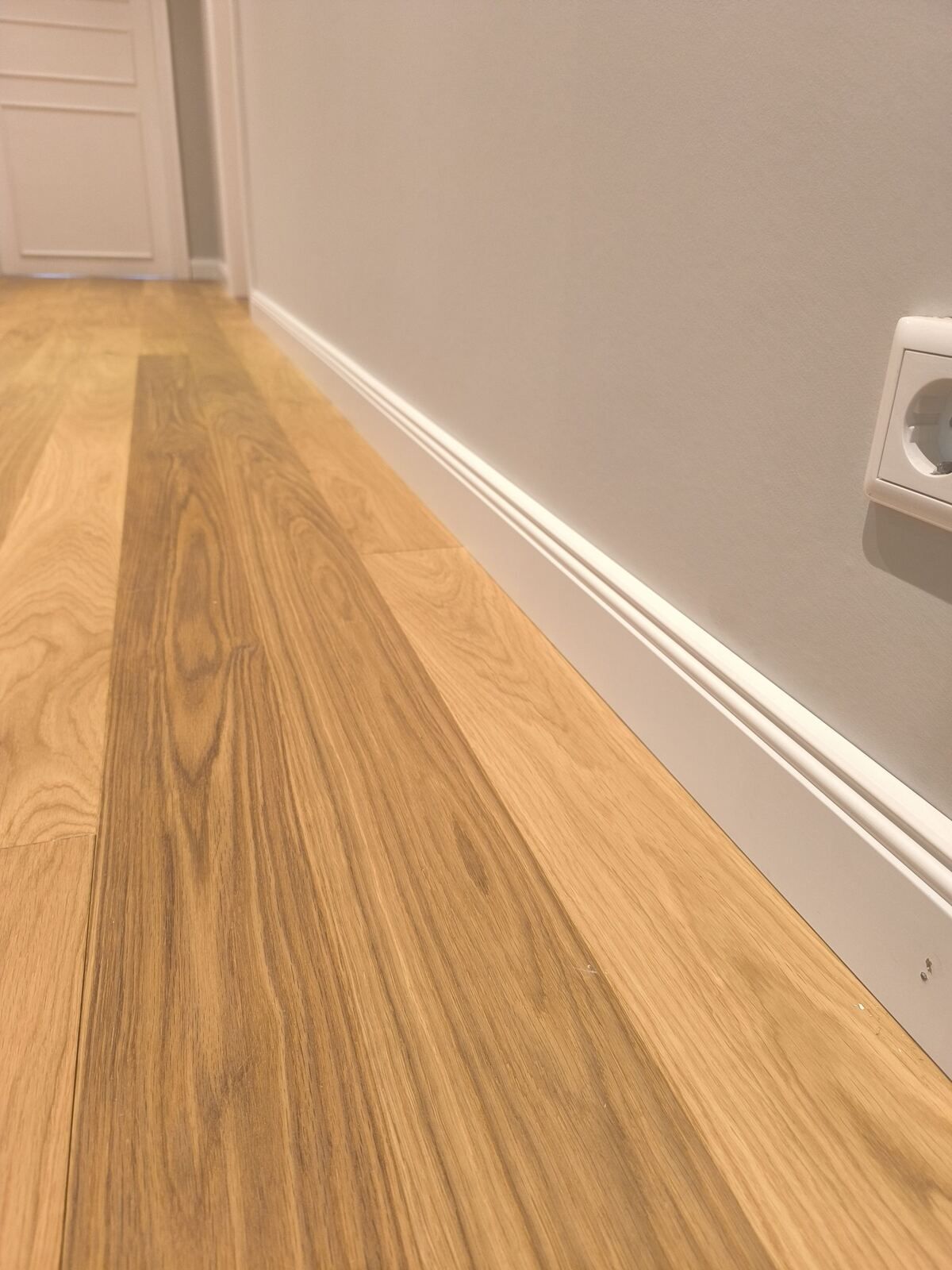 Eine Nahaufnahme eines Holzbodens neben einer Wand mit einer Steckdose.