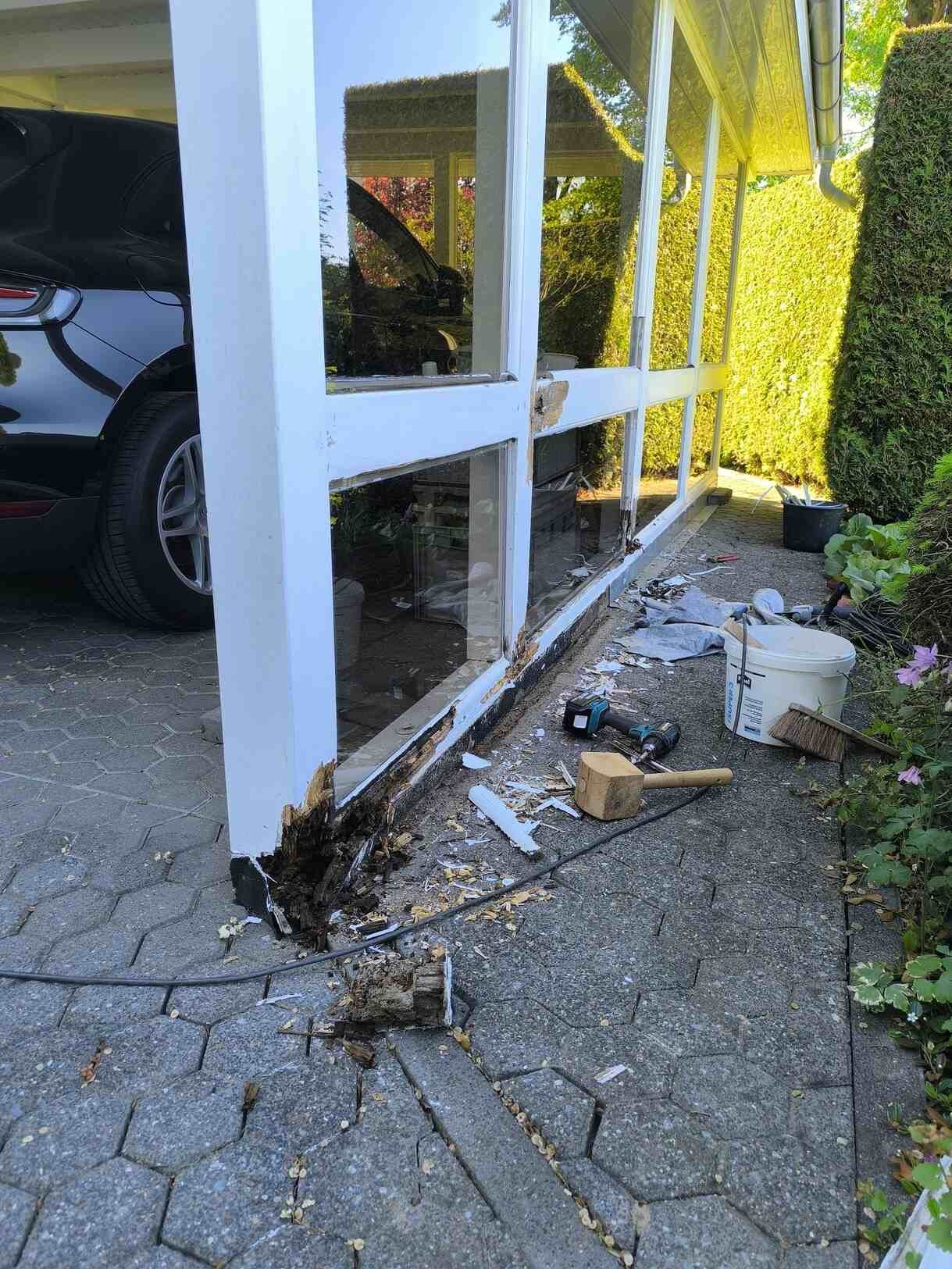 In einer Einfahrt ist neben einem zerbrochenen Fenster ein Auto geparkt.
