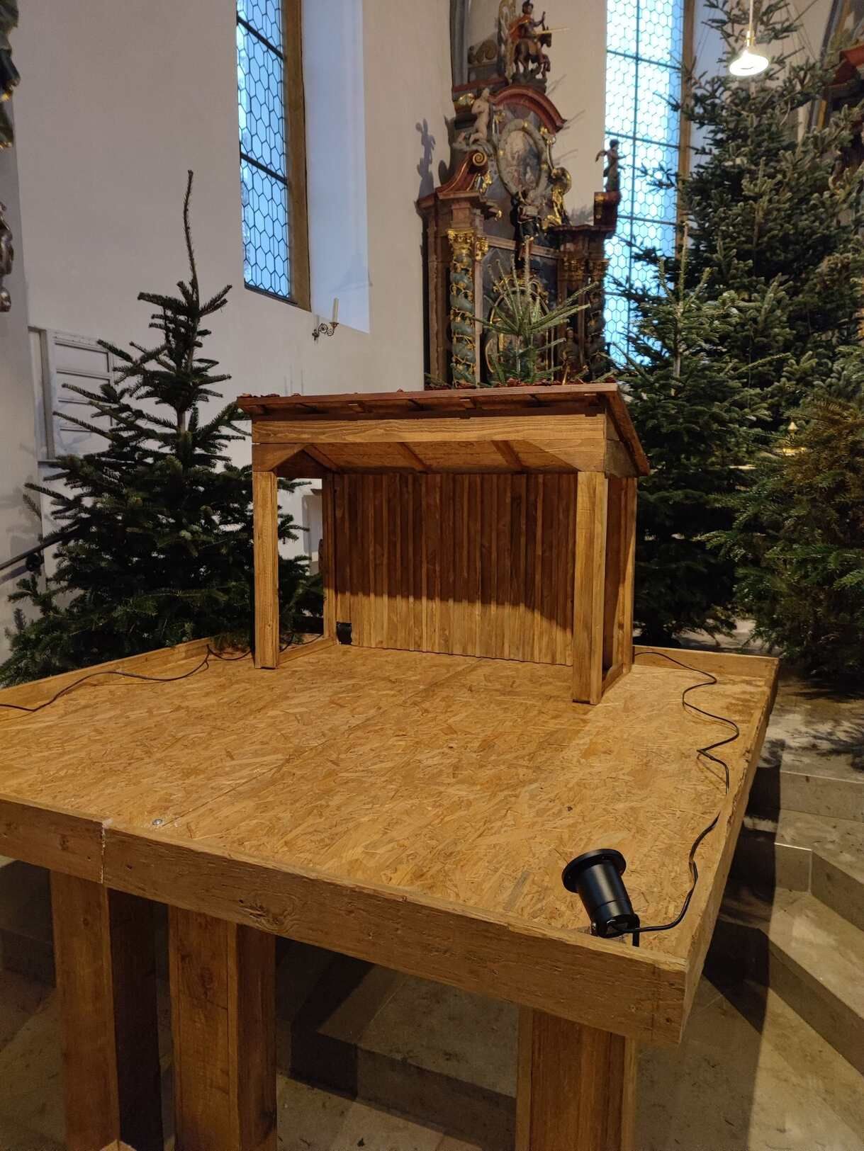 Ein Holztisch in einer Kirche mit Weihnachtsbäumen im Hintergrund.