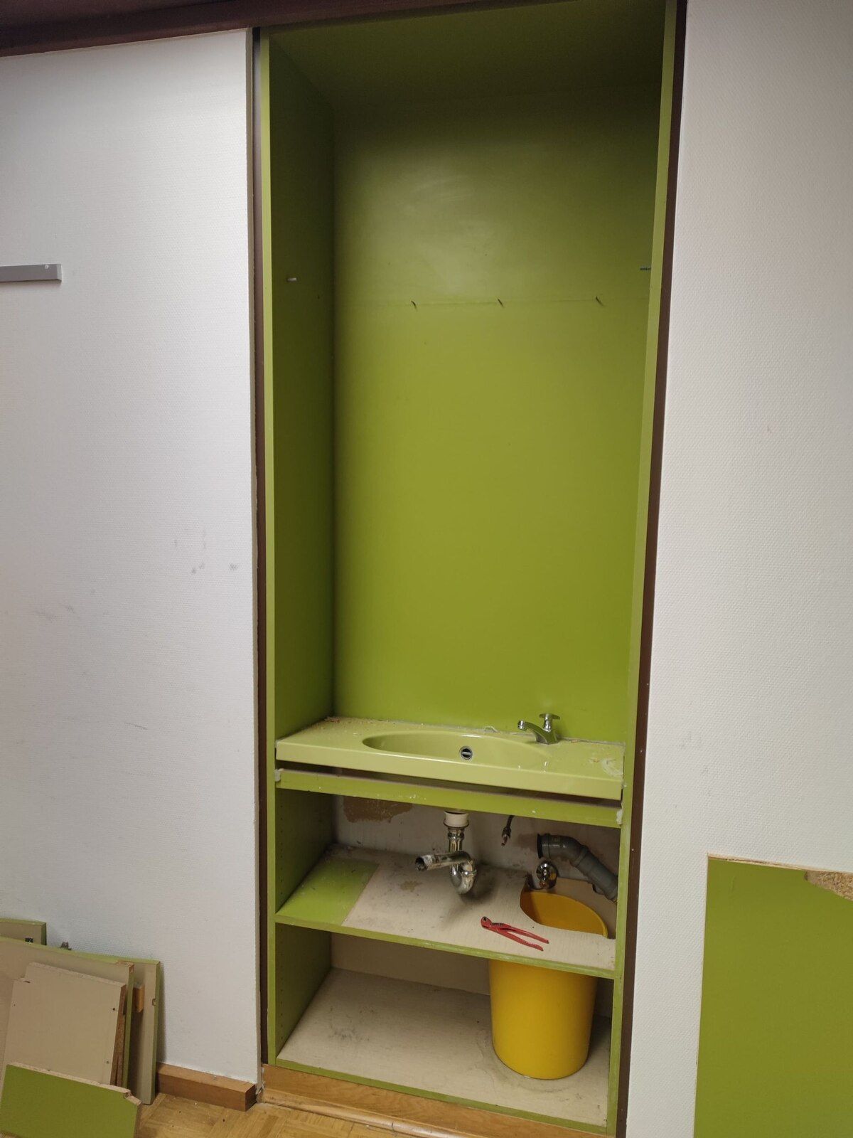 Ein grüner Schrank mit einem Waschbecken und einem gelben Eimer auf dem Regal