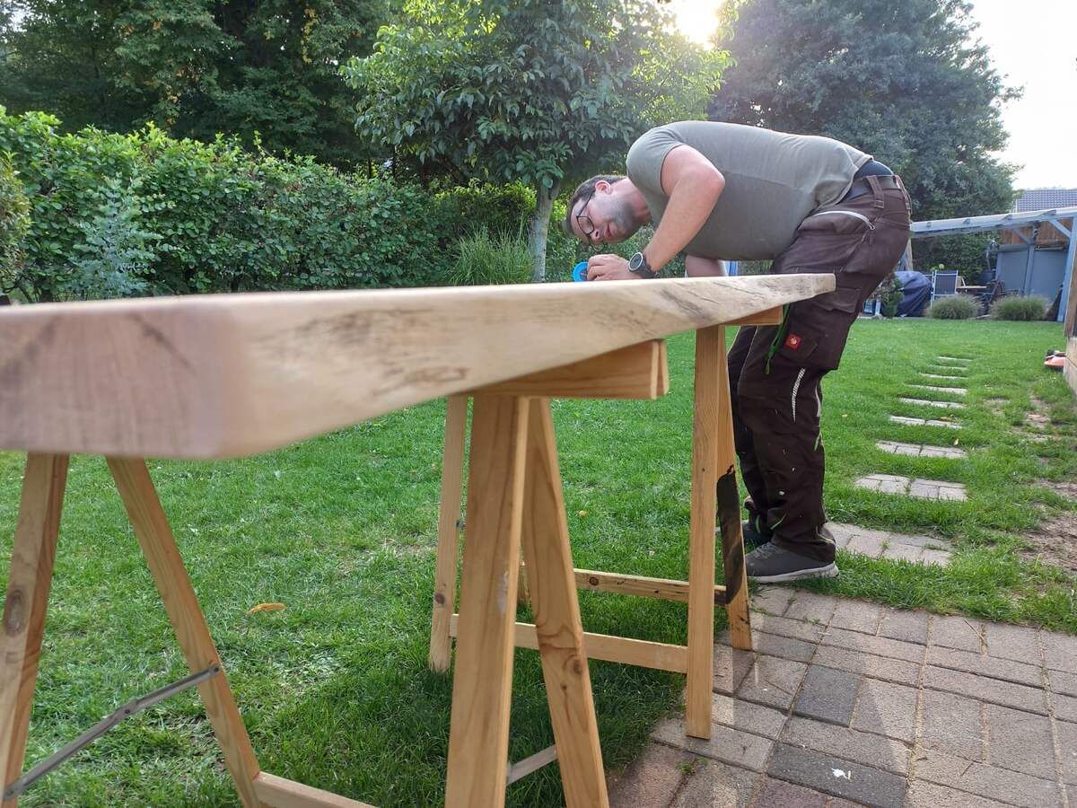 Ein Mann beugt sich in einem Hof über einen Holztisch.