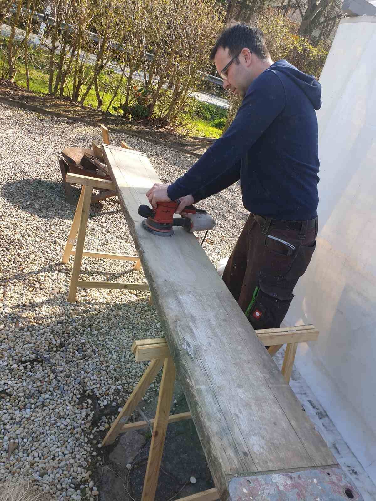 Ein Mann schleift mit einer Schleifmaschine ein Stück Holz.