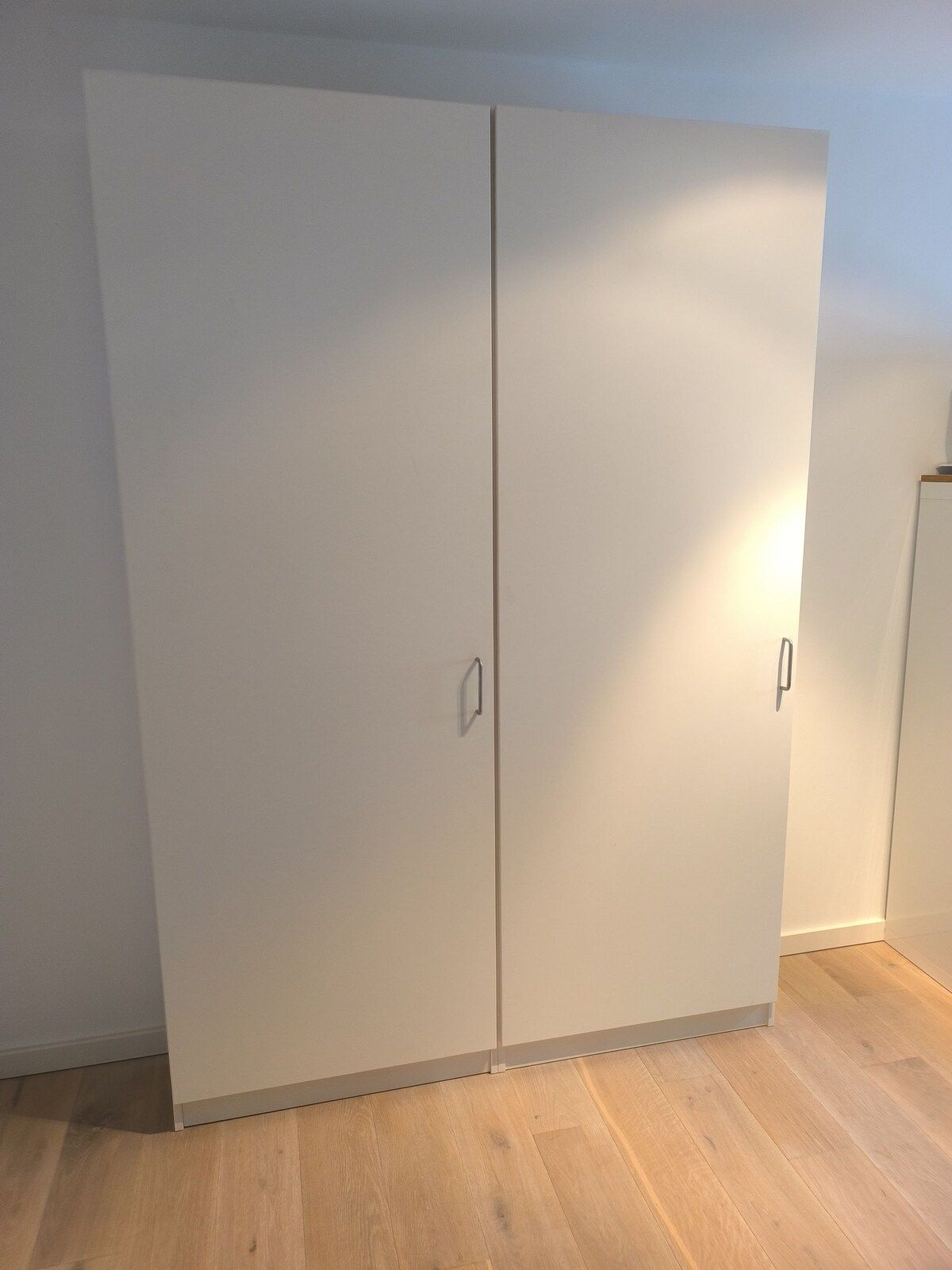 In der Mitte eines Raumes steht ein großer weißer Kleiderschrank.