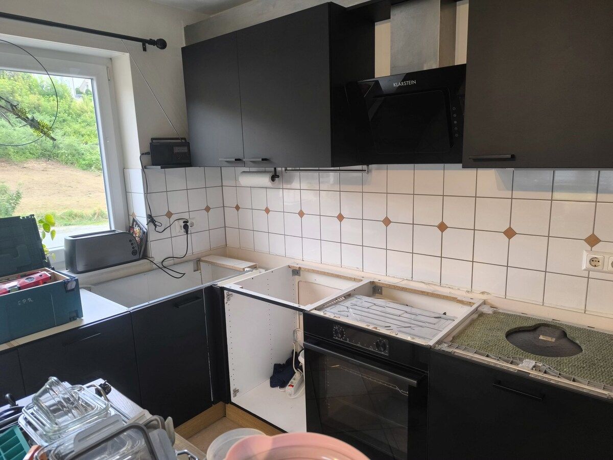 Eine Küche mit schwarzen Schränken, einem Herd, einer Spüle und einem Fenster.