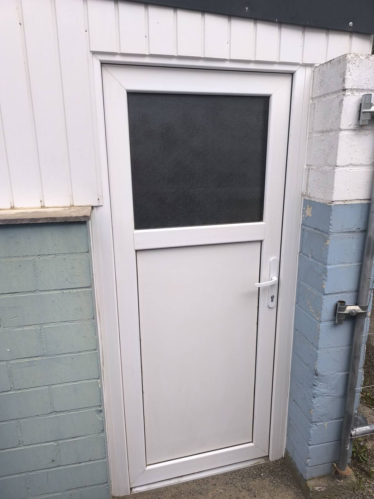 An der Seite eines Gebäudes befindet sich eine weiße Tür mit einem Glasfenster.