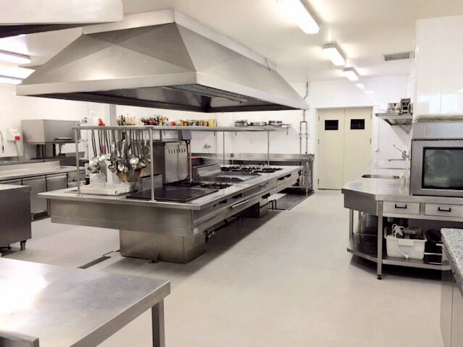 Cocina comercial con electrodomésticos de acero inoxidable y ventilación superior.