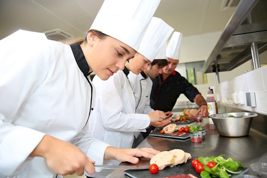 Chefs con uniformes y sombreros blancos preparando comida en una cocina comercial.