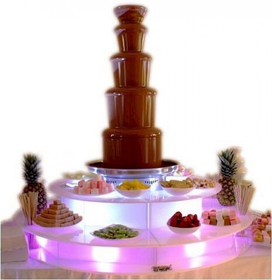 Fuente de chocolate con delicias para mojar en una exhibición escalonada iluminada.