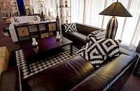 Sala de estar con sofás de cuero negro, almohadas geométricas y una mesa de café negra.