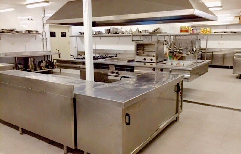 Cocina comercial con encimeras, electrodomésticos y campana extractora de acero inoxidable.