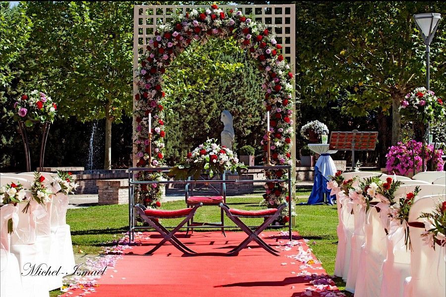 Montaje de ceremonia de boda al aire libre con arco floral, sillas y alfombra roja.