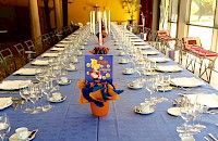 Mesa larga dispuesta para evento formal con mantel azul, cristalería y centro de mesa.