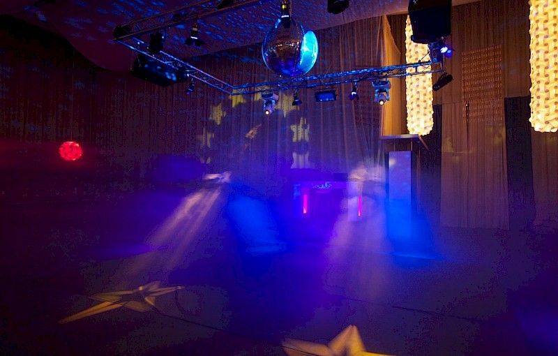 Un escenario iluminado con luces azules y rojas, una bola de discoteca y un símbolo de estrella de la Unión Europea