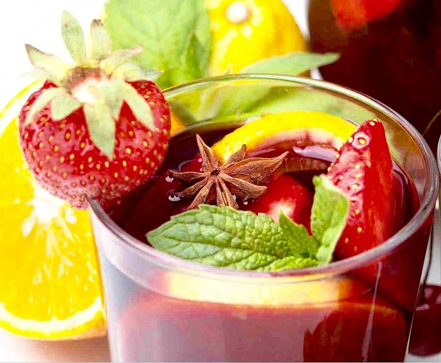 Primer plano de sangría con fresas, rodaja de naranja, limón, menta y anís estrellado.