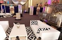 Espacio para eventos con muebles blancos, alfombra geométrica en blanco y negro, barra y acentos decorativos.