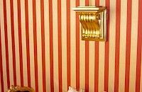 Aplique de pared dorado sobre papel pintado de rayas rojas y crema.