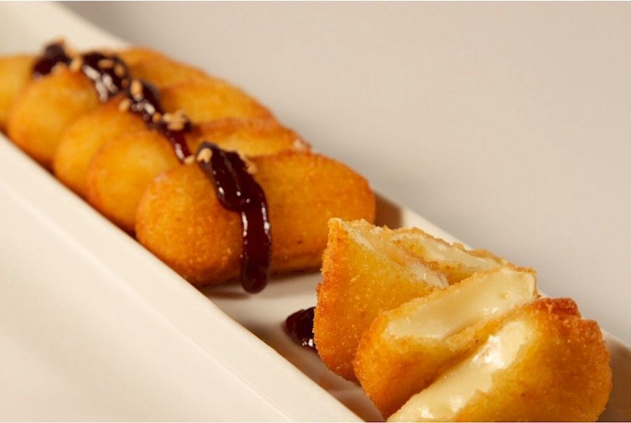 Bolas de queso fritas doradas con salsa oscura rociadas sobre un plato blanco.
