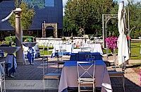 Espacio para eventos al aire libre con mesas con mantelería azul y gris. Al fondo se ven un edificio y árboles.
