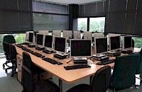 Laboratorio de computación con múltiples monitores, teclados y sillas dispuestas alrededor de una mesa larga .