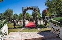 Instalación de ceremonia de boda al aire libre con arco floral, alfombra roja y detalles blancos en un día soleado.