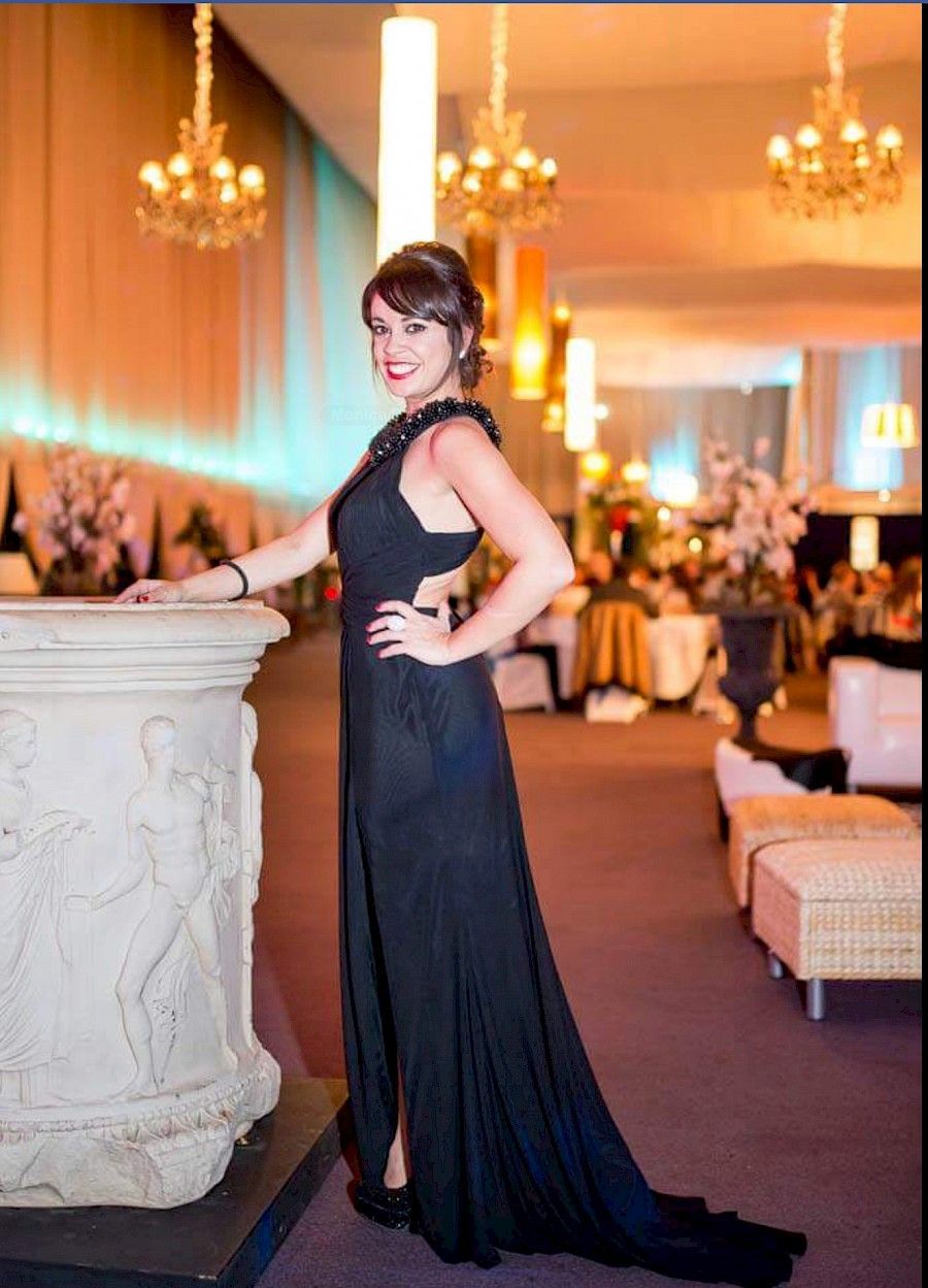 Una mujer con un vestido de noche negro posa junto a una columna en un evento formal.