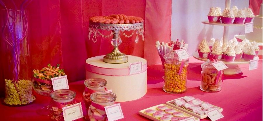 Una mesa de postres rosa con cupcakes, dulces y galletas.