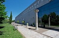 Vista exterior de un edificio moderno con una columna romana, probablemente un museo o centro cultural.