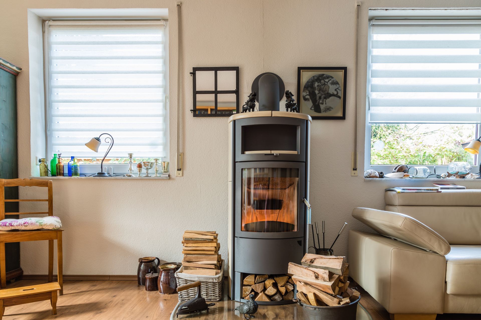 Salon chaleureux avec cheminée allumée, bois de chauffage et deux fenêtres avec stores.