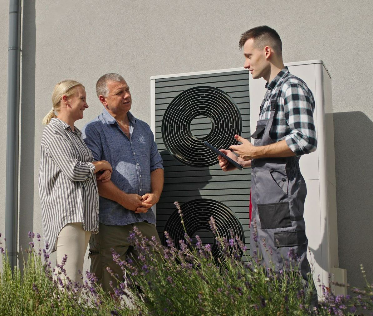 Un technicien utilise une tablette pour démontrer les fonctionnalités d'une pompe à chaleur à un couple, à l'extérieur.