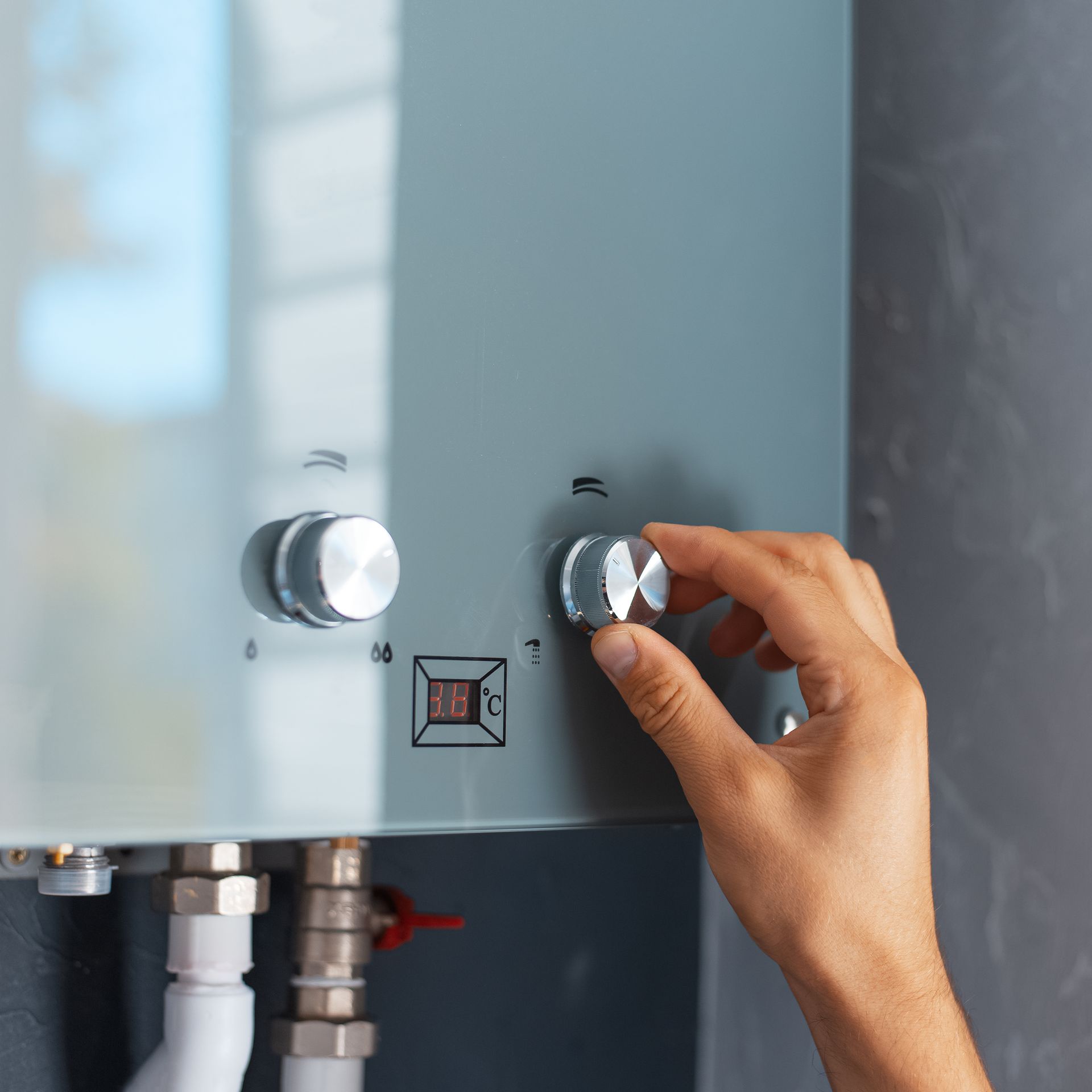 Main tournant un cadran sur un chauffe-eau gris monté sur un mur gris.