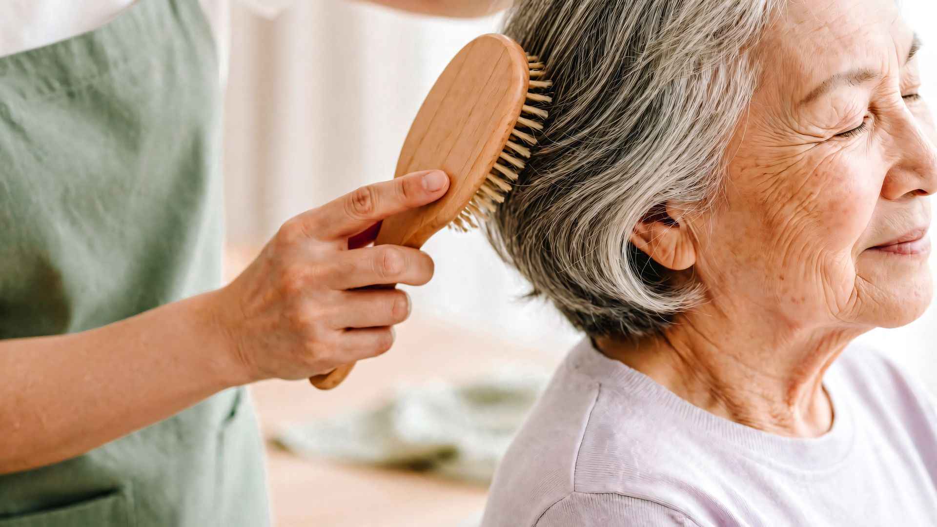 Une personne coiffe les cheveux gris d'une personne âgée avec une brosse en bois.