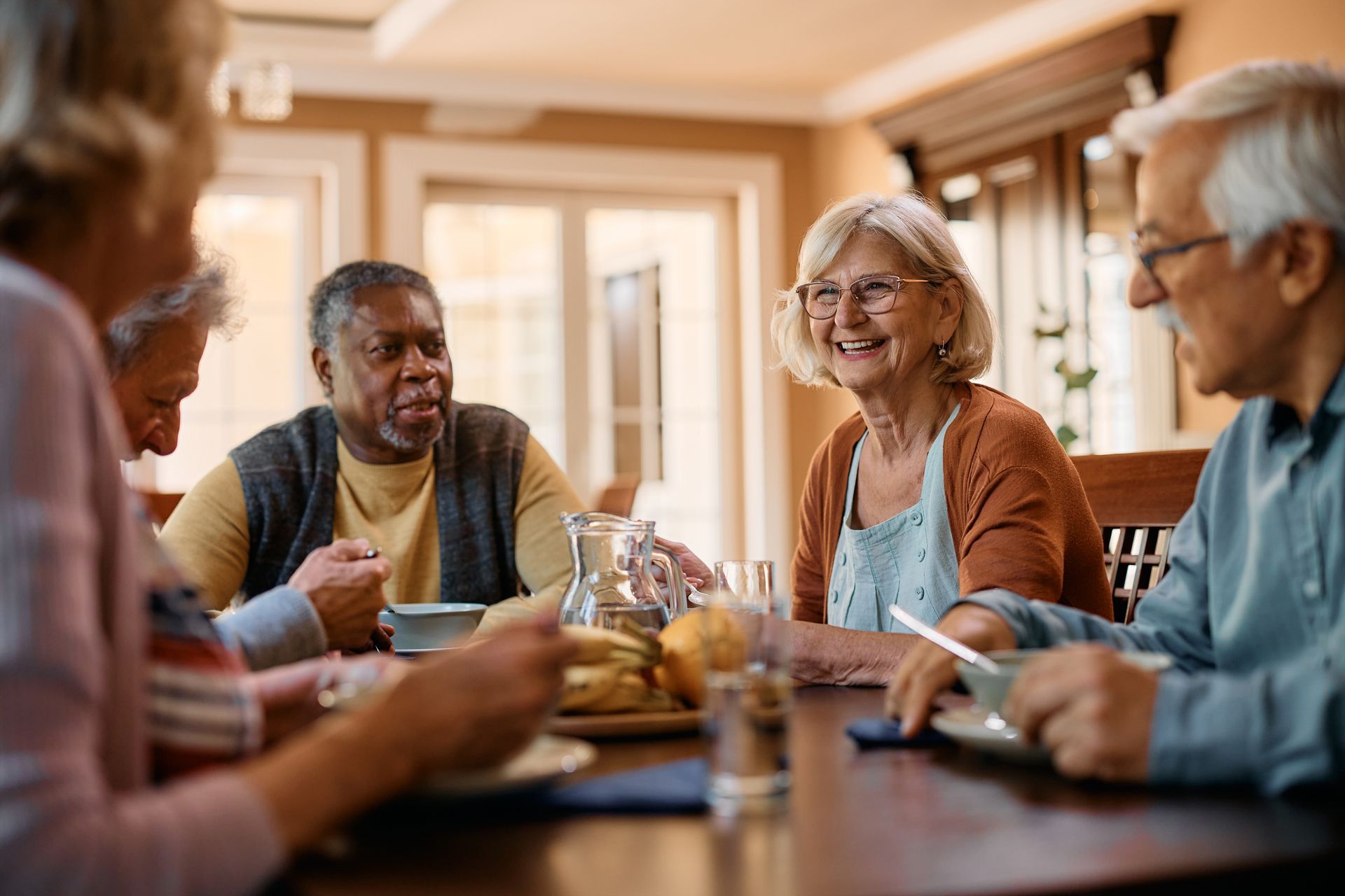 Des amis discutent autour d'un verre à une table à manger dans une pièce lumineuse et confortable