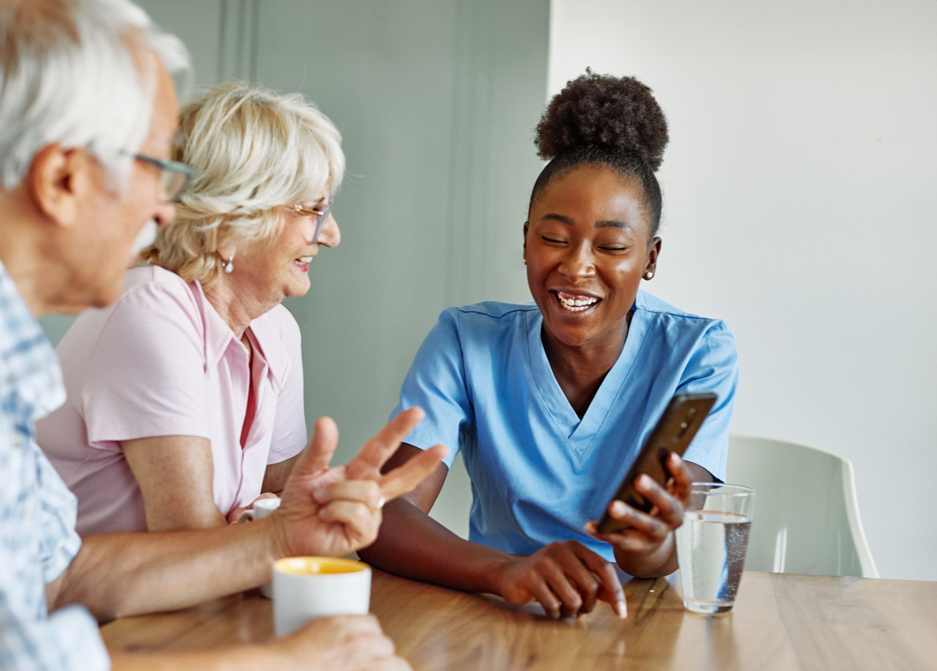 Trois personnes sourient et discutent à une table, l'une d'elles montre l'écran de son smartphone.