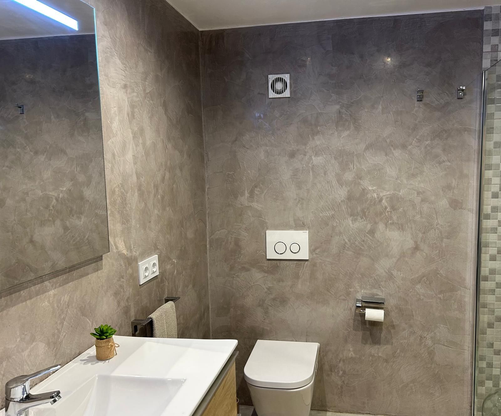 Bany amb parets amb aspecte de marbre gris, vàter, lavabo i zona de dutxa.