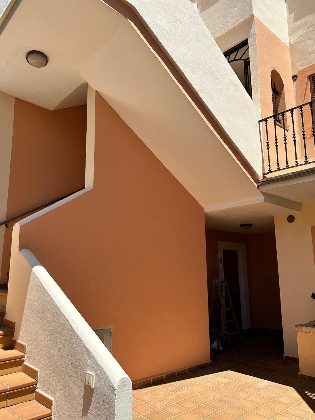 Vista exterior d'un edifici de color préssec amb escales, porta i balcó.