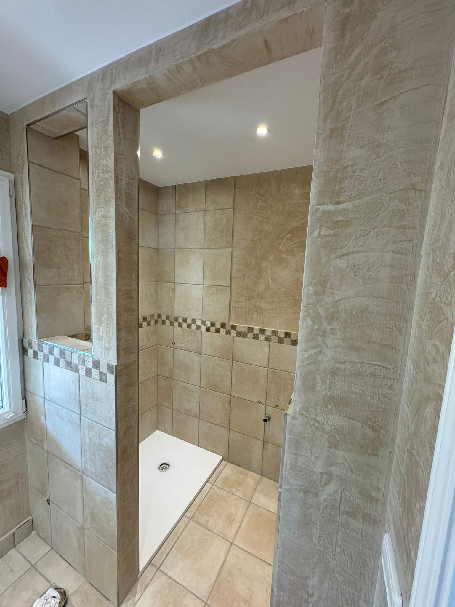 Bany amb parets de rajoles, dutxa a ras de terra amb base blanca i il·luminació encastada.